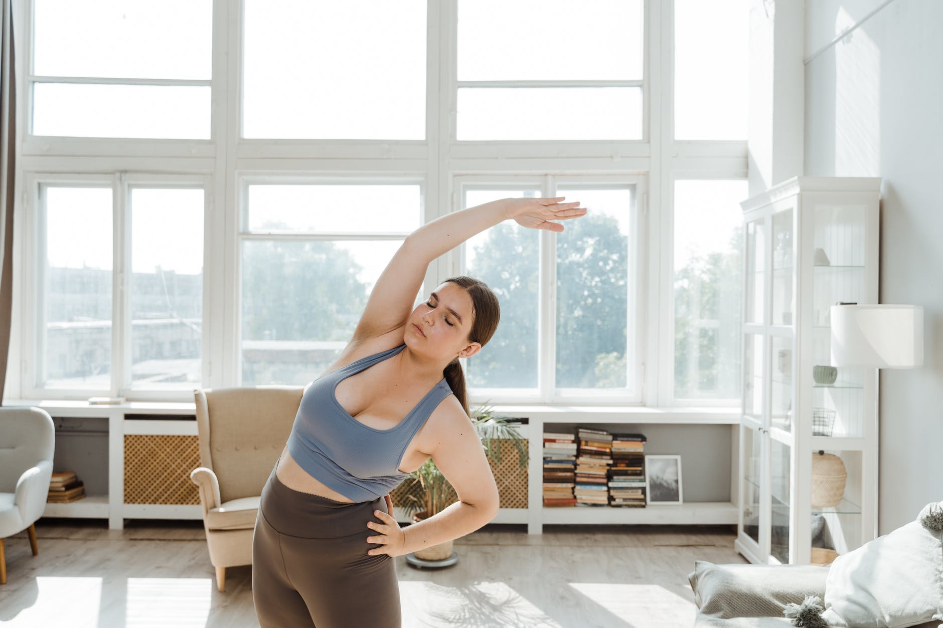 woman in blue sports bra and gray leggings doing exercises in the room with big window Losing weight